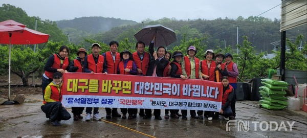 복숭아 밭 앞에서 기념촬영을 하고 있는 윤사모 대구동구 봉사단원들과 최성덕 회장이 우산을 쓰고 있는 모습.